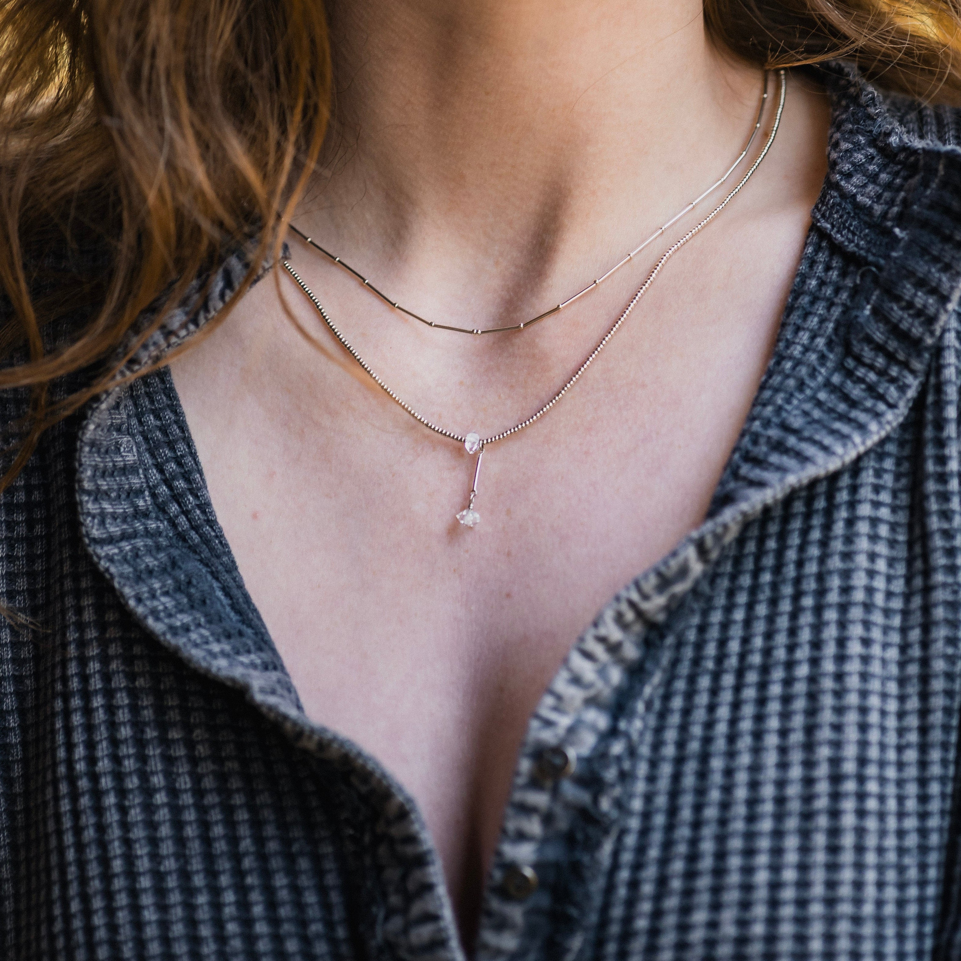 Close-up of a person wearing a delicate necklace with a textured shirt.
