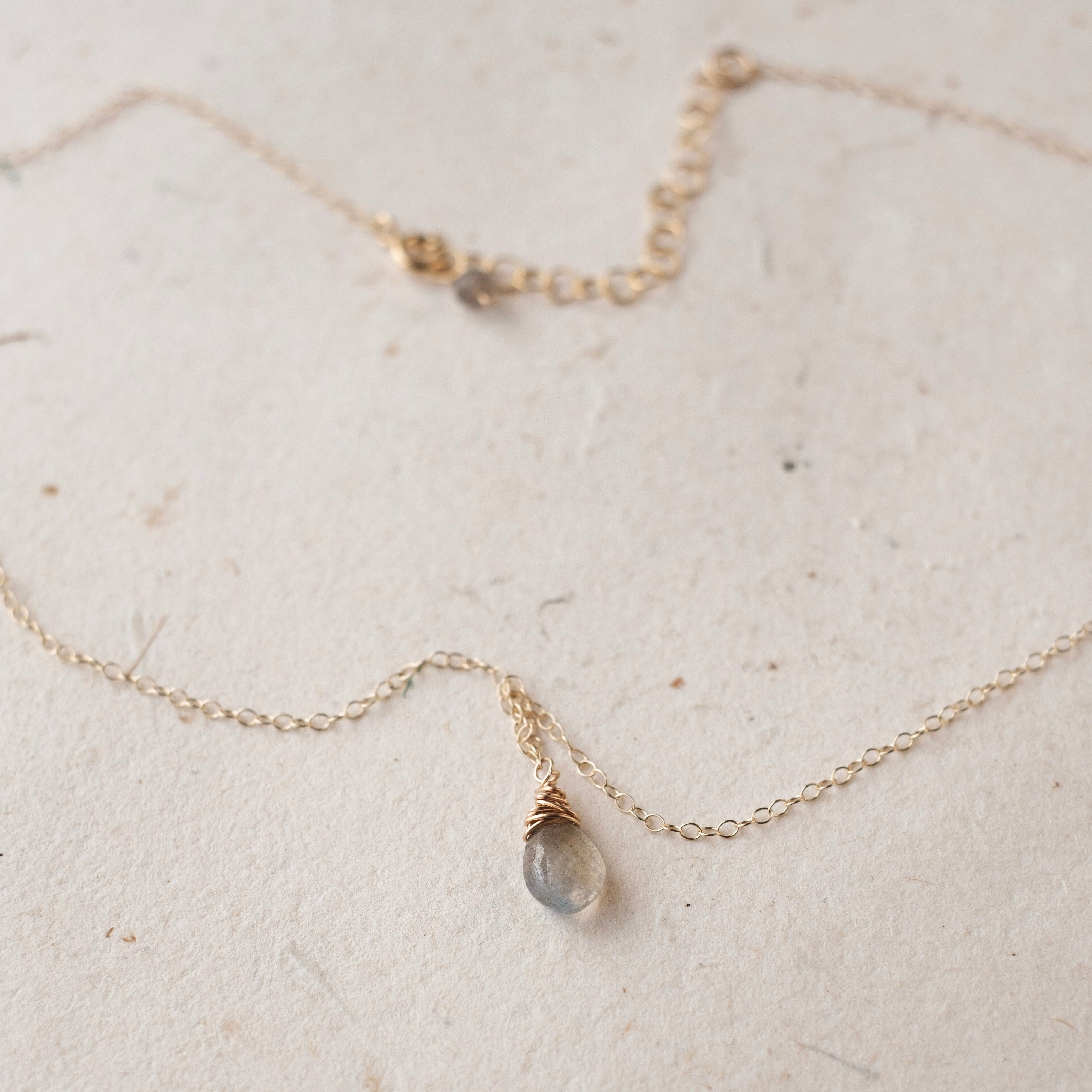 Delicate gold necklace with a small gemstone on a textured beige surface