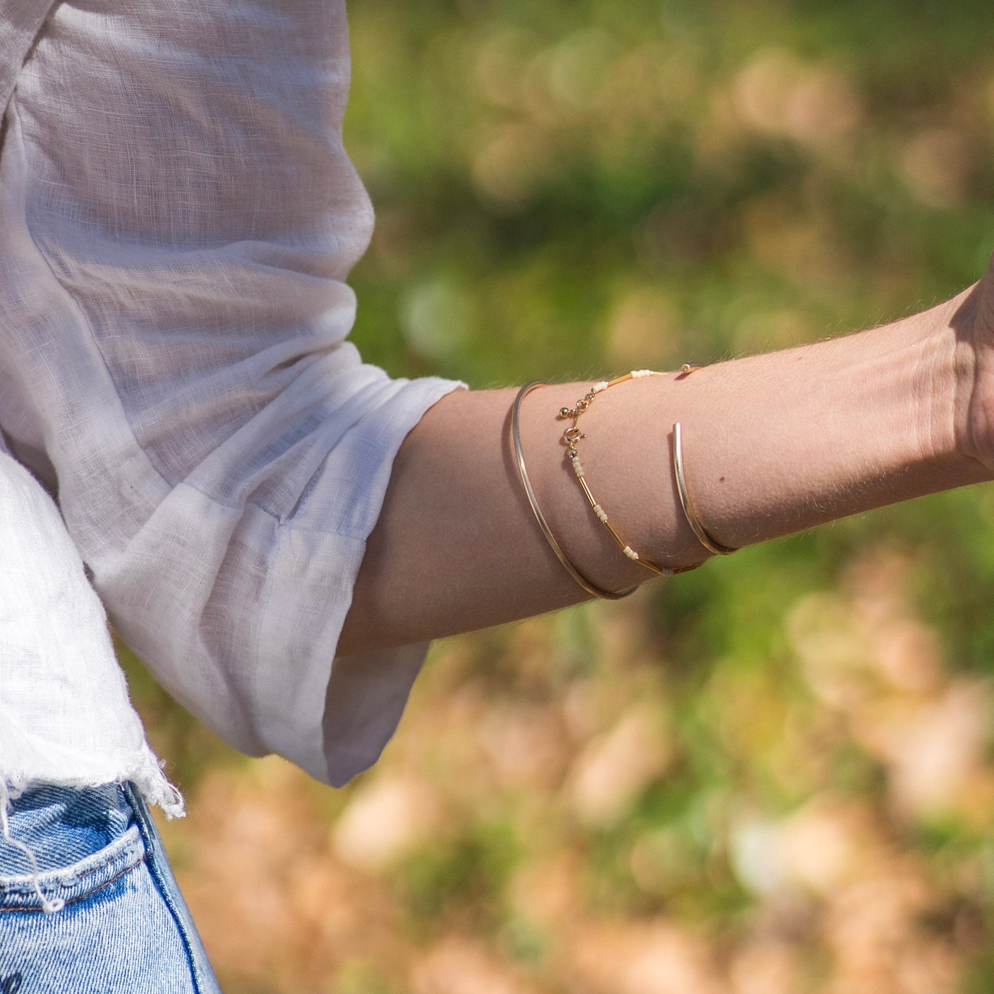 Person wearing gold bracelets on a blurred natural background