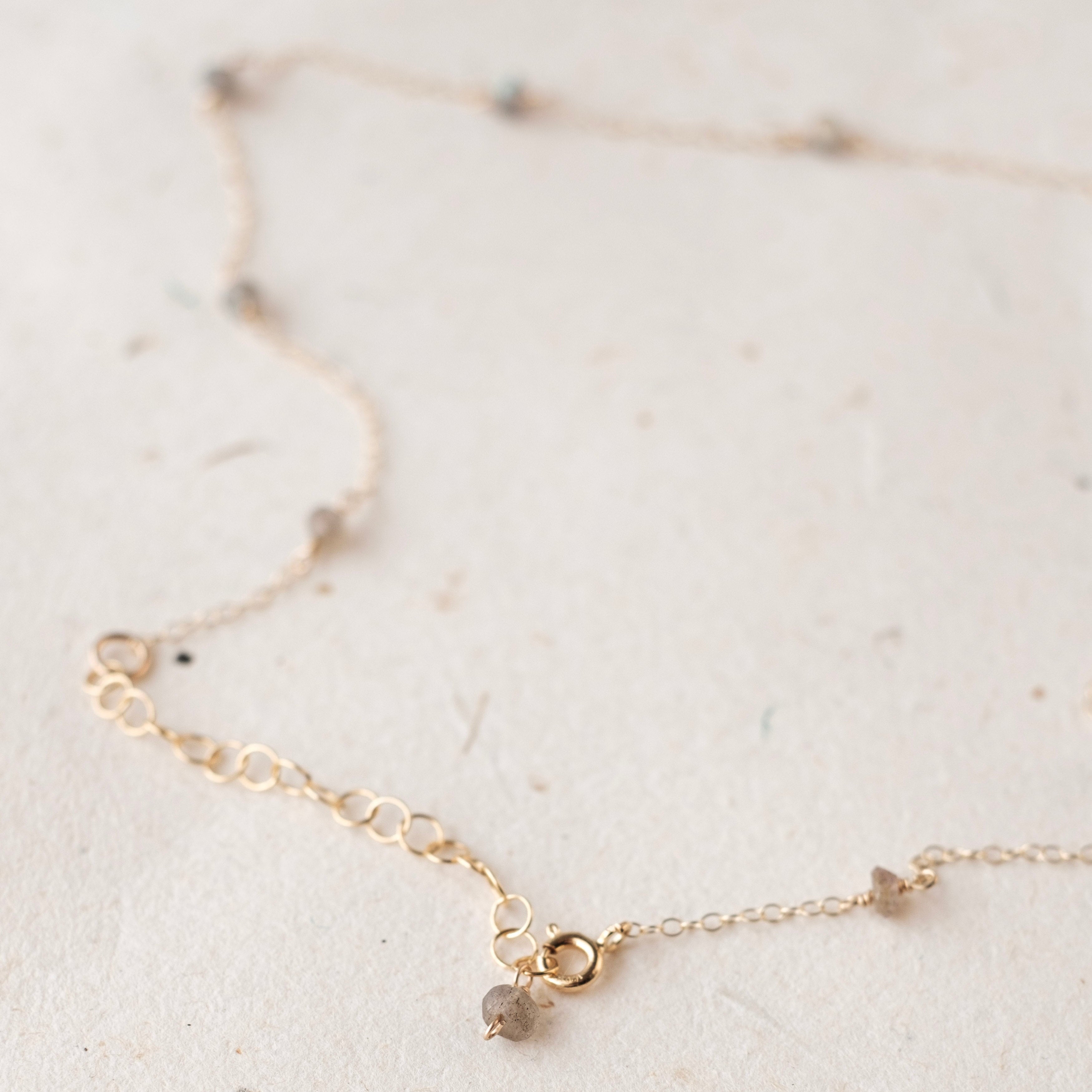 Delicate gold necklace with small gemstones on a light background
