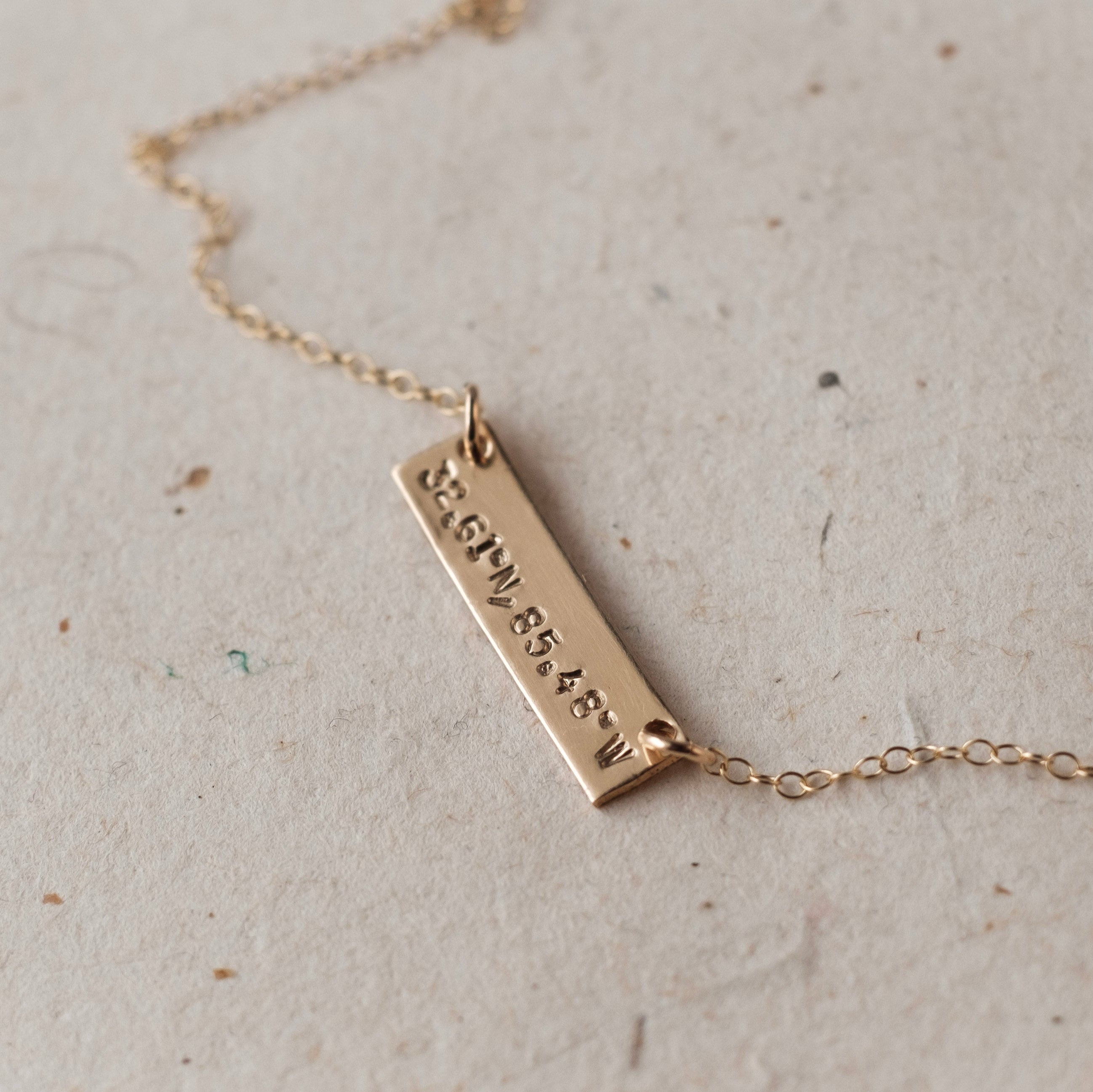 Gold necklace with a bar pendant on a light gray background