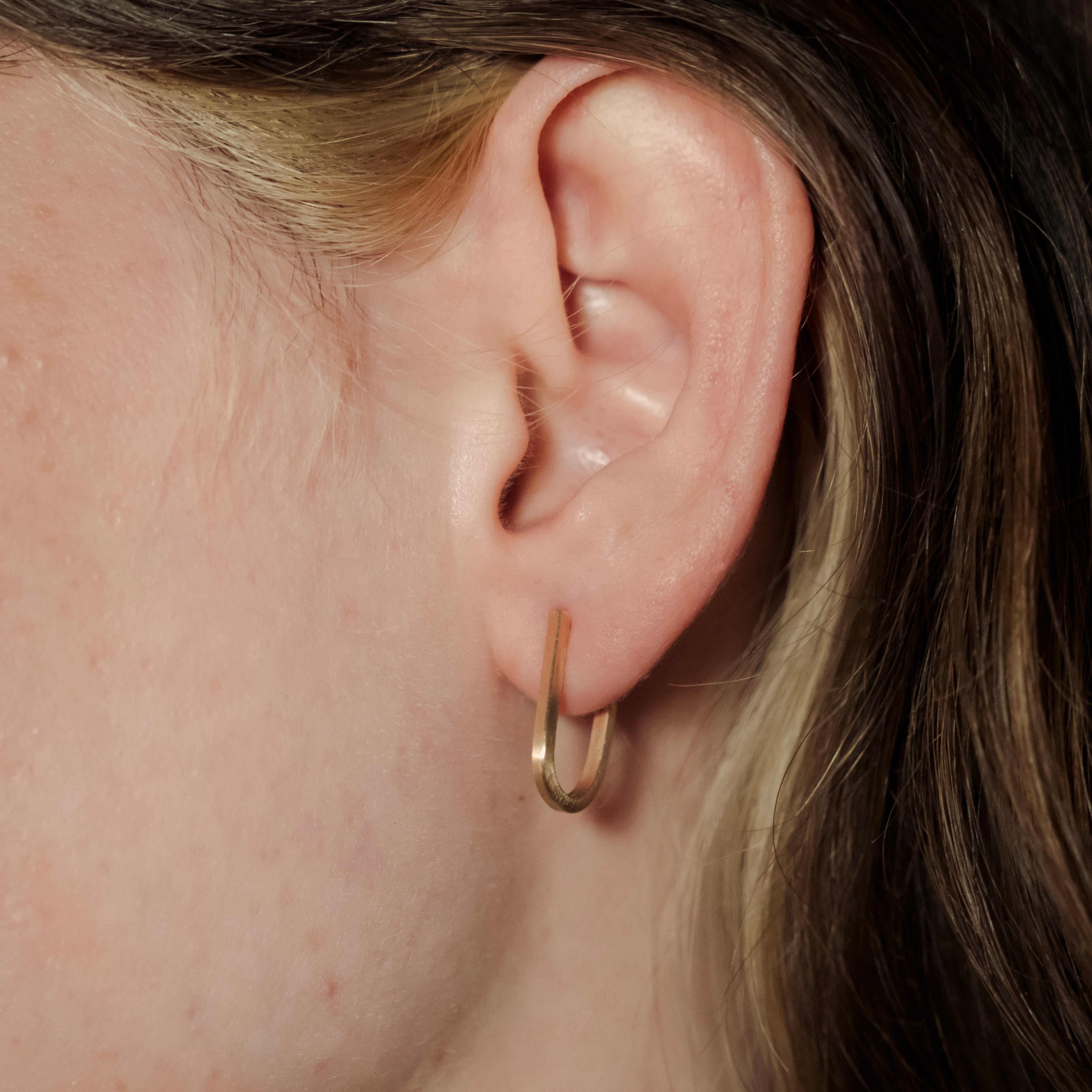 Close-up of an ear wearing a gold hoop earring with a blurred background