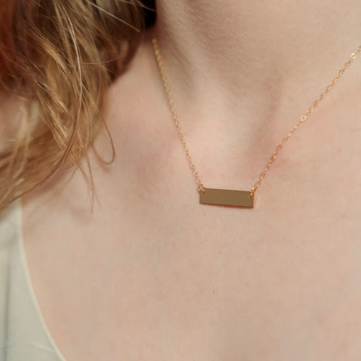 Gold necklace with a rectangular pendant on a person's neck
