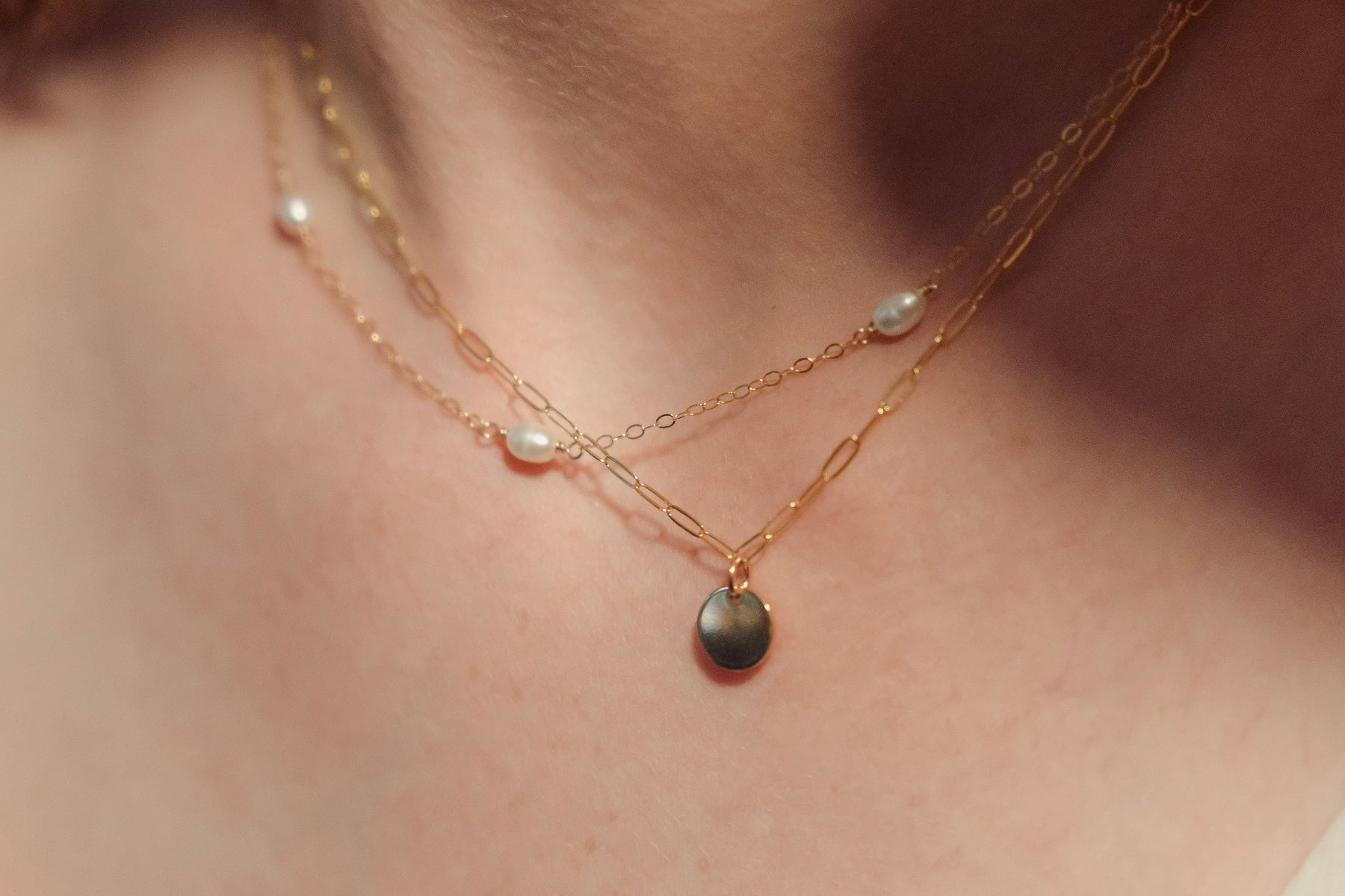 Gold necklace with pearl pendants on a person's neck against a neutral background