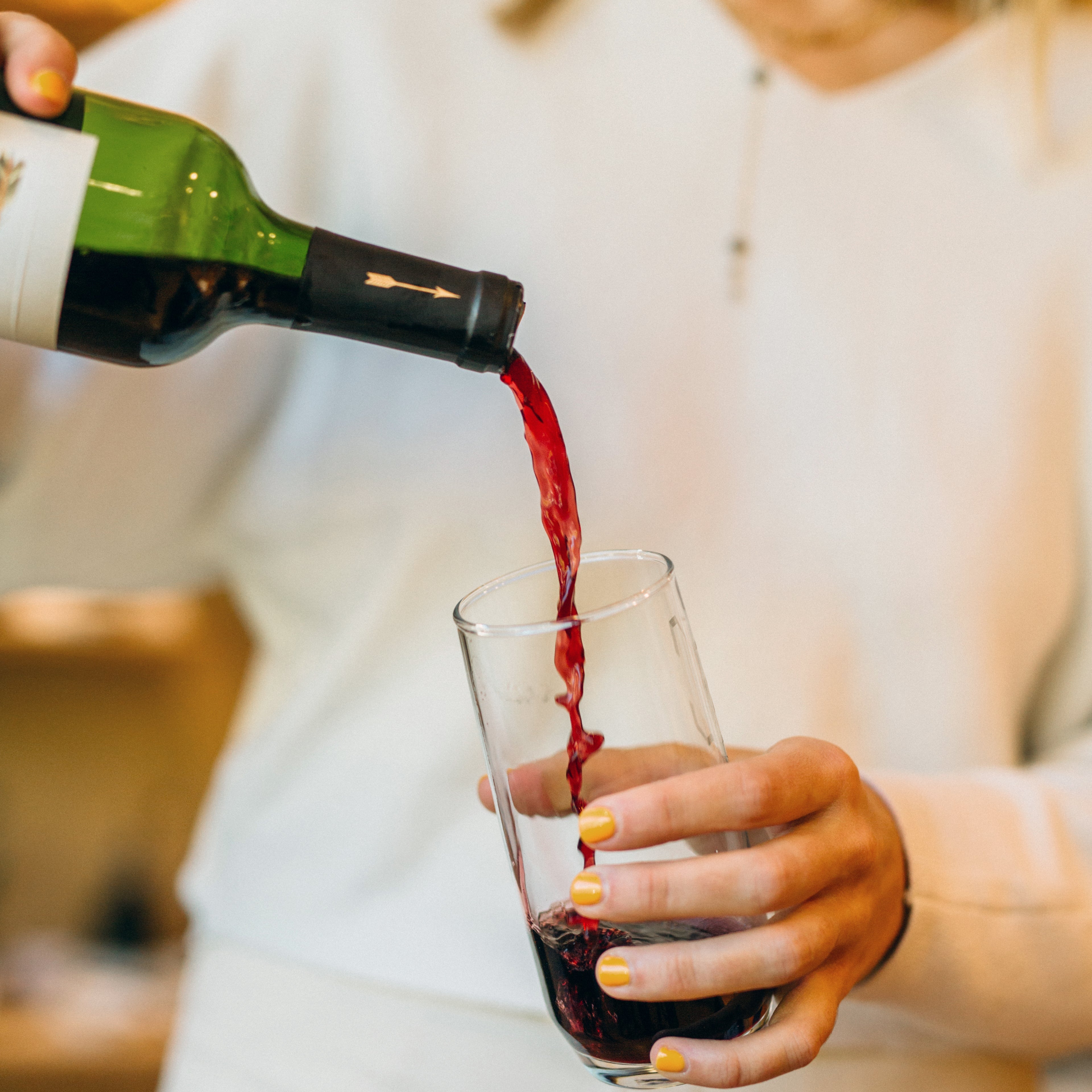 Person pouring red wine into a glass with a blurred background