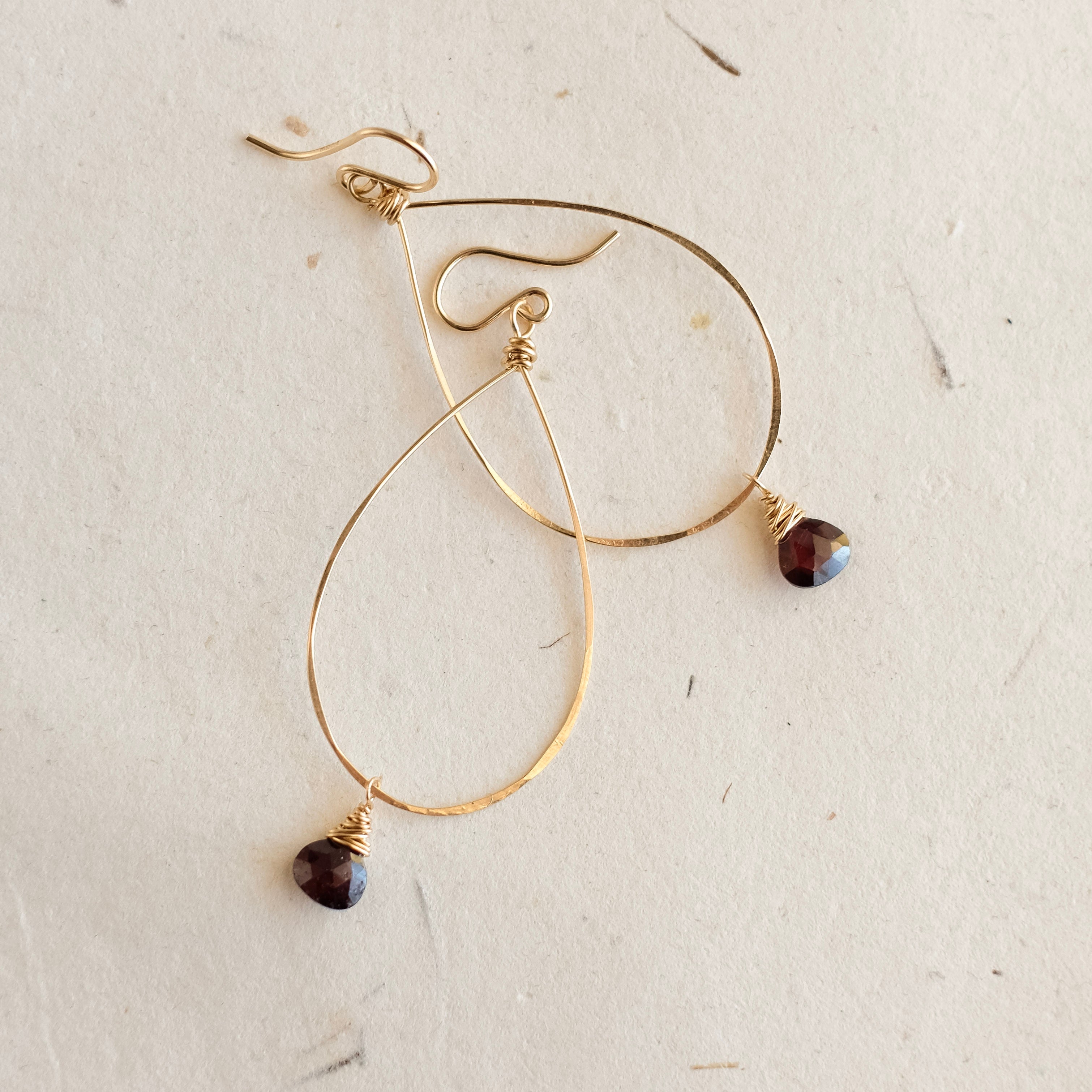 Gold hoop earrings with dark beads on a textured beige surface