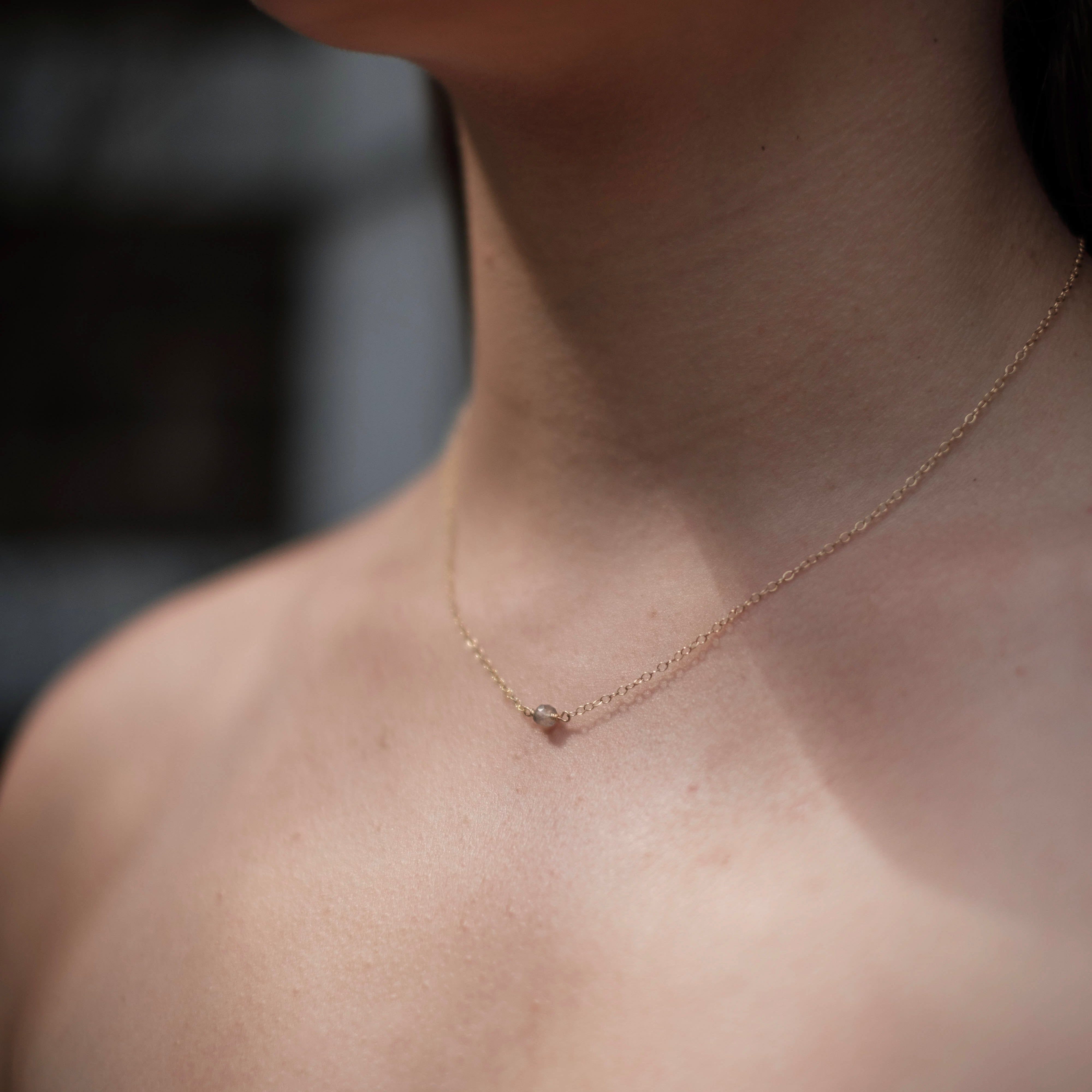 Close-up of a person wearing a delicate necklace with a blurred background