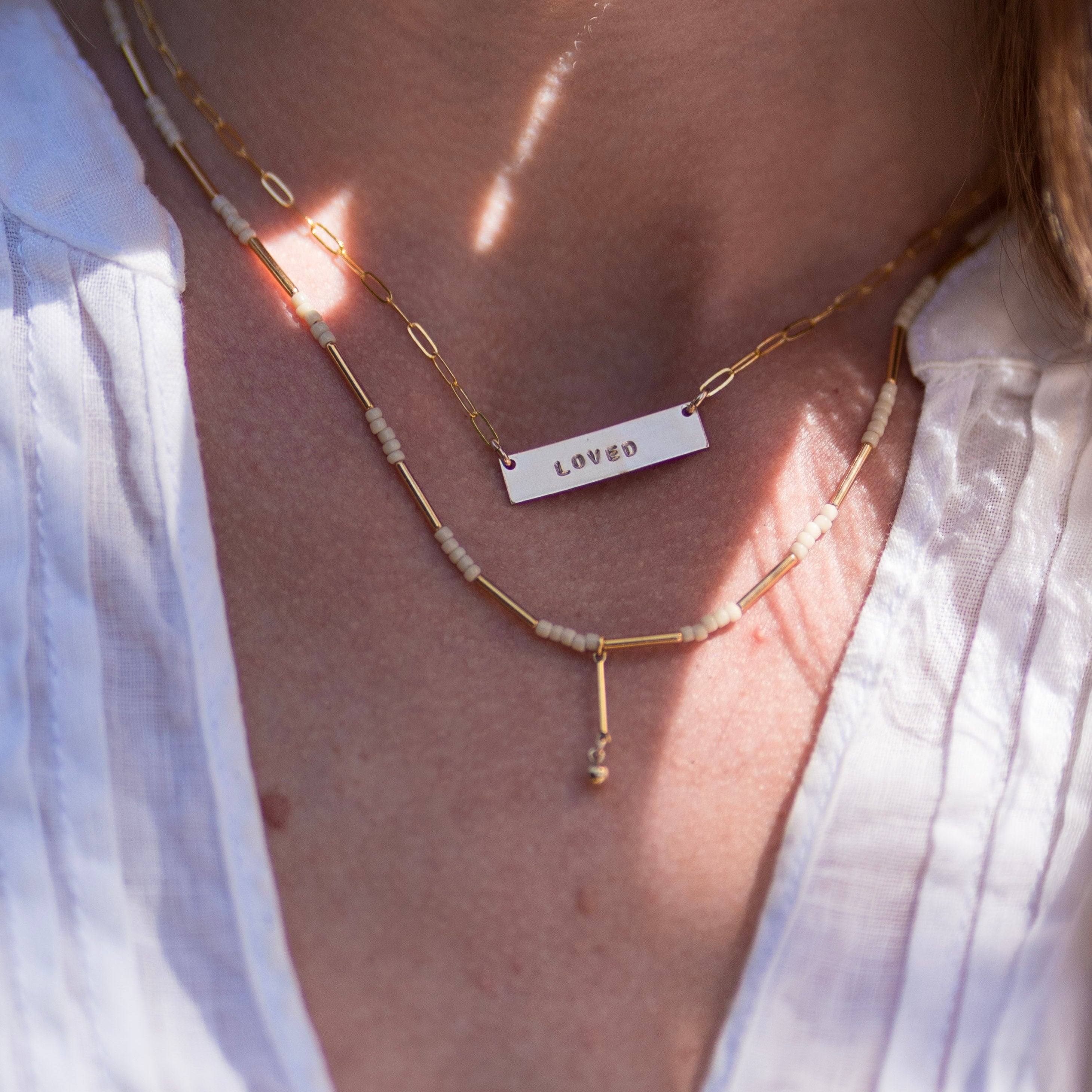 Gold necklace with a 'LOVED' pendant on a person wearing a white shirt.