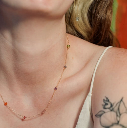 Necklace with small beads worn by a person with a tattoo on their shoulder.