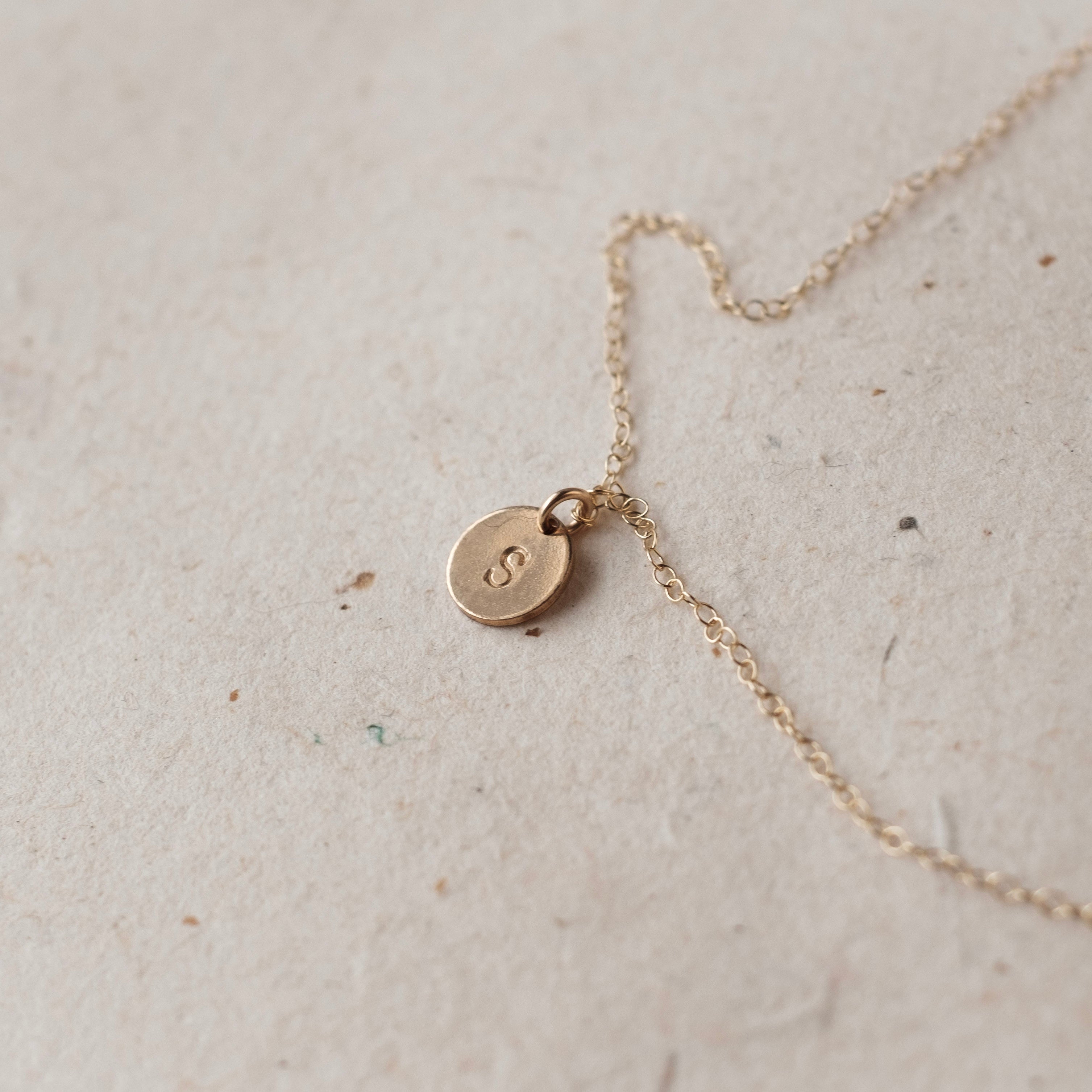 Gold necklace with a small round pendant on a light beige surface