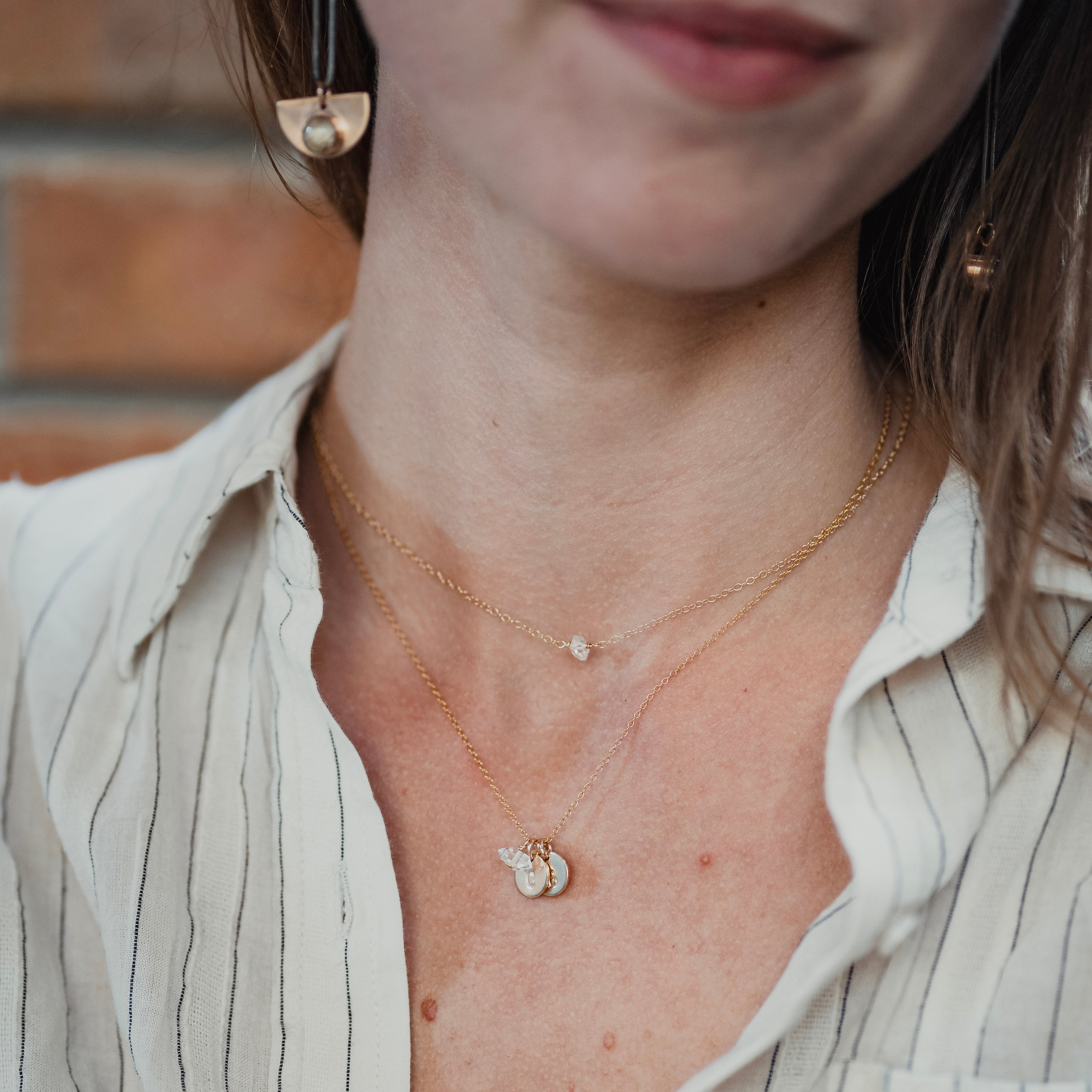 Close-up of a person wearing a delicate necklace with a small pendant, set against a neutral background.