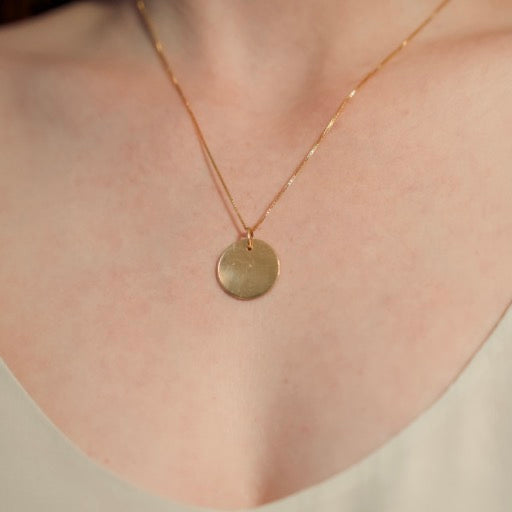 Gold necklace with a round pendant on a person wearing a white top.